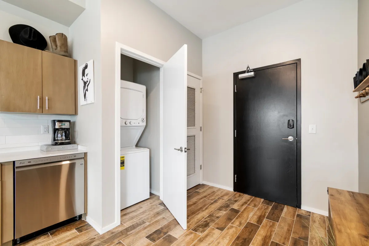 This image features a modern kitchen area with cabinets, an in-unit washer and dryer, and a coffee maker. The contemporary black door hints at secure, access-controlled entry. The scene is practical and welcoming, suggesting both comfort and efficiency for guests balancing work and daily routines.