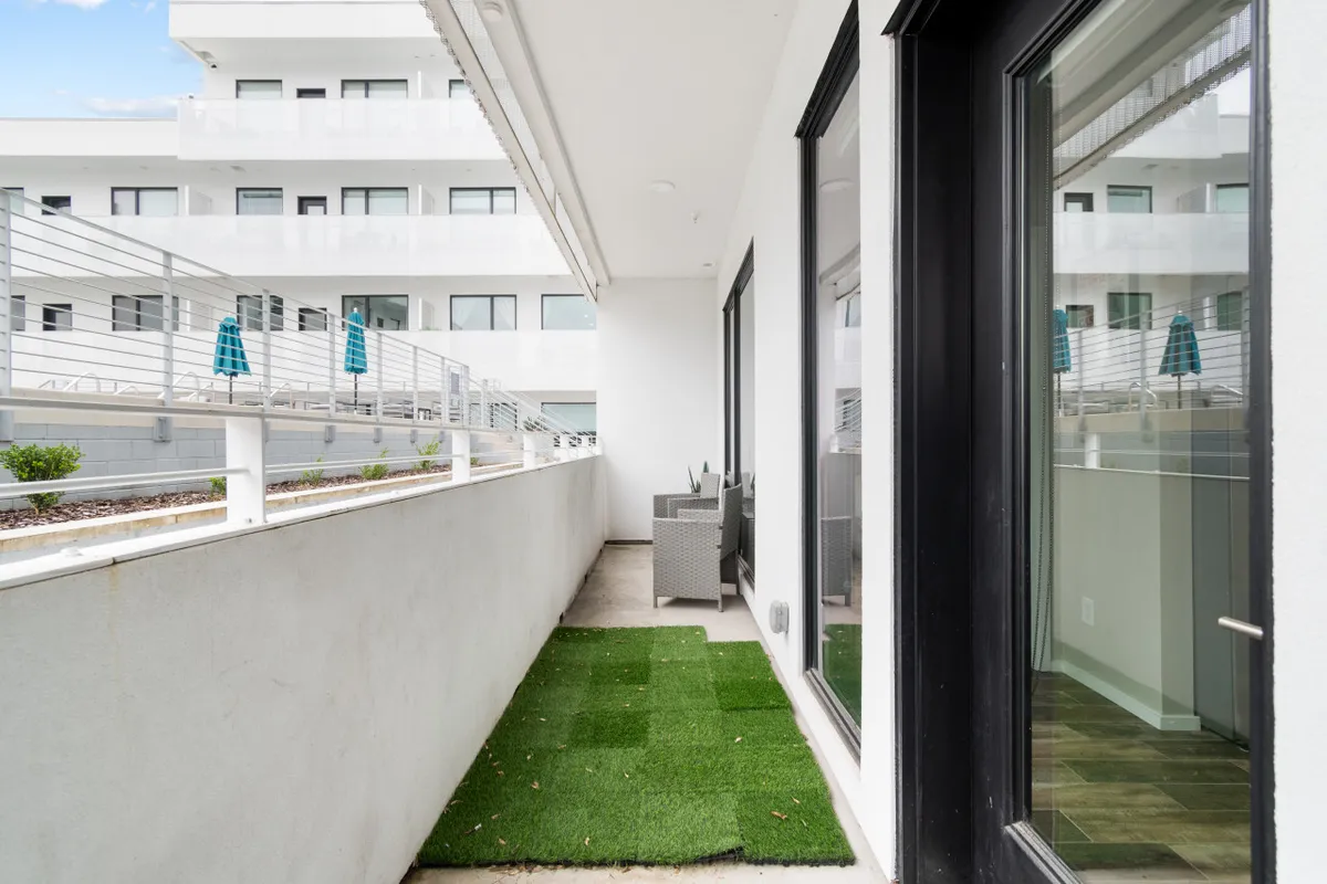 This image showcases an inviting synthetic grass area with outdoor seating and large windows, creating a seamless connection between the interior and the patio. The space is sunlit and designed for relaxation, offering an ideal spot for morning coffee or evening gatherings.