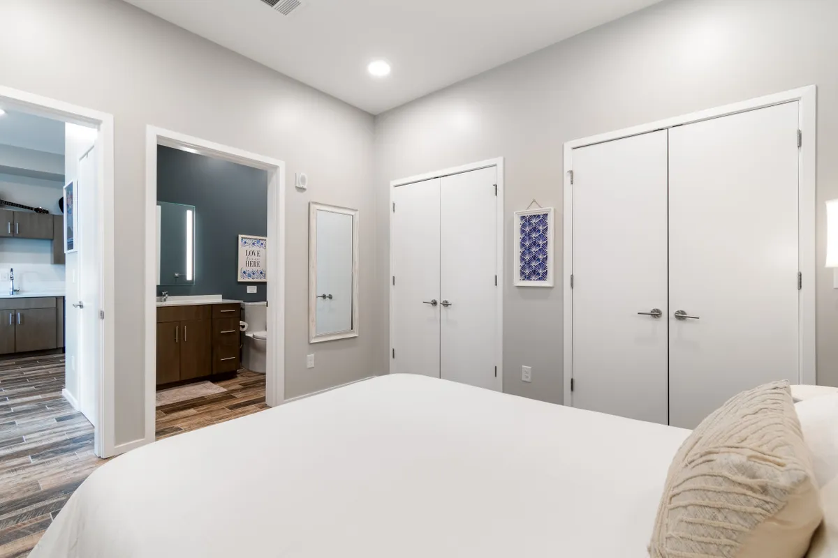 A calm bedroom with a decorative pillow on the bed, a mirrored wall reflecting the space, and double closets. The soft lighting creates a welcoming environment ideal for preparing for a day of exploring Nashville or resting after family activities.