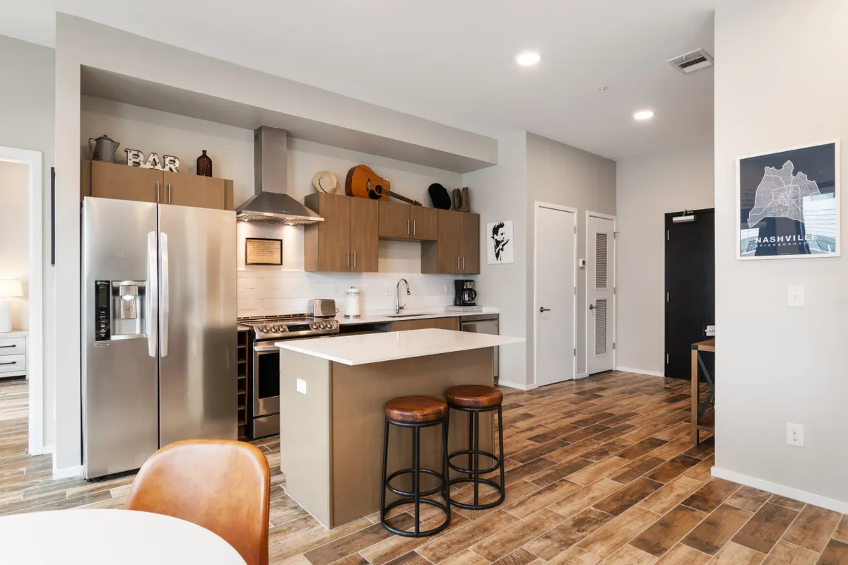 A stylish kitchen with a central island, stainless steel appliances, and bar stools, designed for both everyday use and social gatherings. The space is modern and inviting, hinting at opportunities to socialize and entertain, such as in a community barbecue lounge or shared meals.