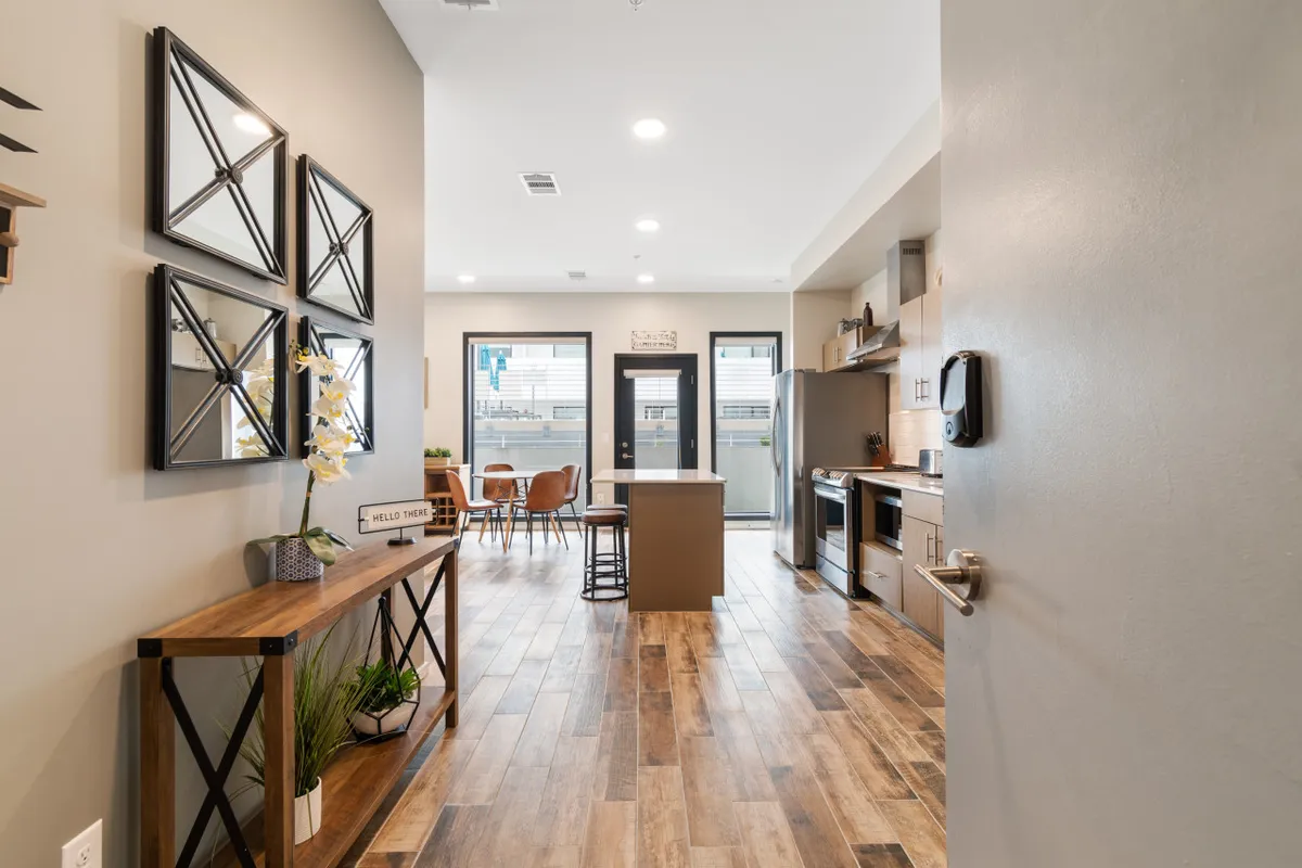 This image captures the open-concept entryway, kitchen, and dining area, with a modern console table, kitchen island, and a dining set for several guests. The view toward the door suggests easy access to outdoor living, making it feel welcoming for group gatherings and celebrations.