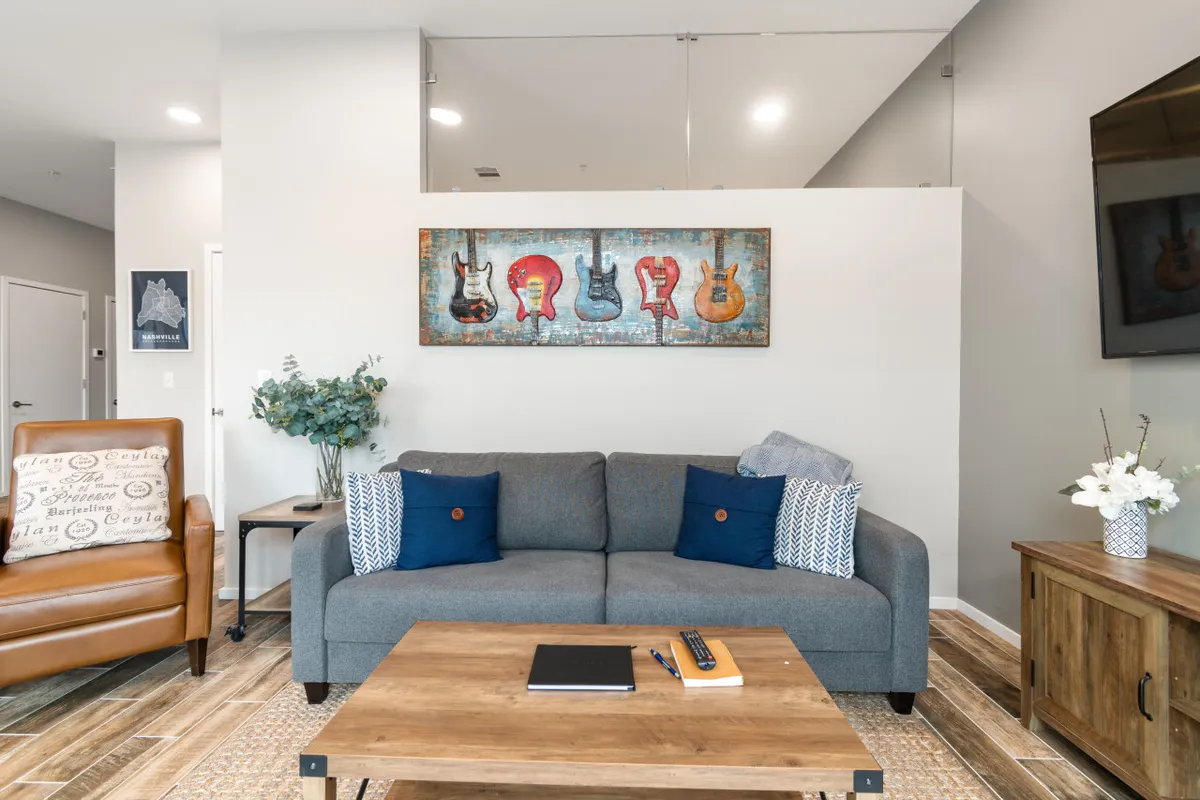 A comfortable living area with a sofa, cushions, guitar-themed artwork, wooden coffee table, television, and a potted plant. The space looks inviting for relaxing, socializing, or enjoying music together, echoing the spirit of group fun and connection.