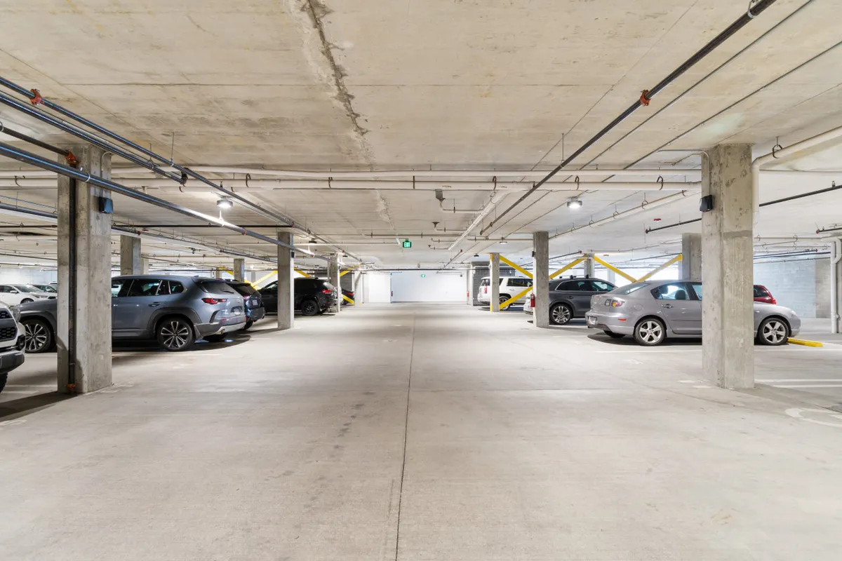 An interior view of a secure, well-lit garage with parked cars and sturdy concrete pillars. The space is clean, organized, and emphasizes ease of access and resident security.