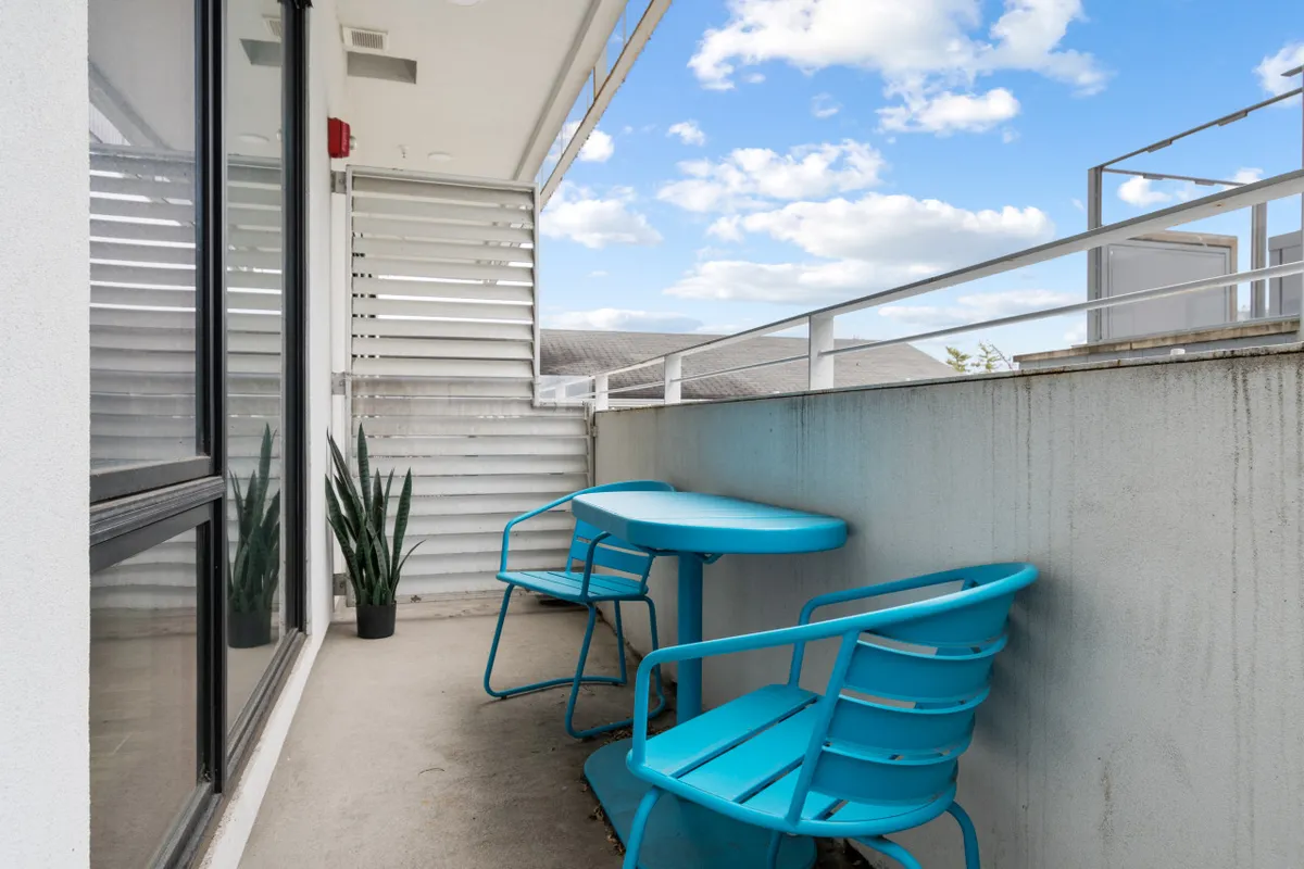 A cozy outdoor setting featuring turquoise chairs around a round table, complemented by a potted plant. The intimate arrangement suggests a space for small gatherings, drinks, or leisurely meals under the sky.