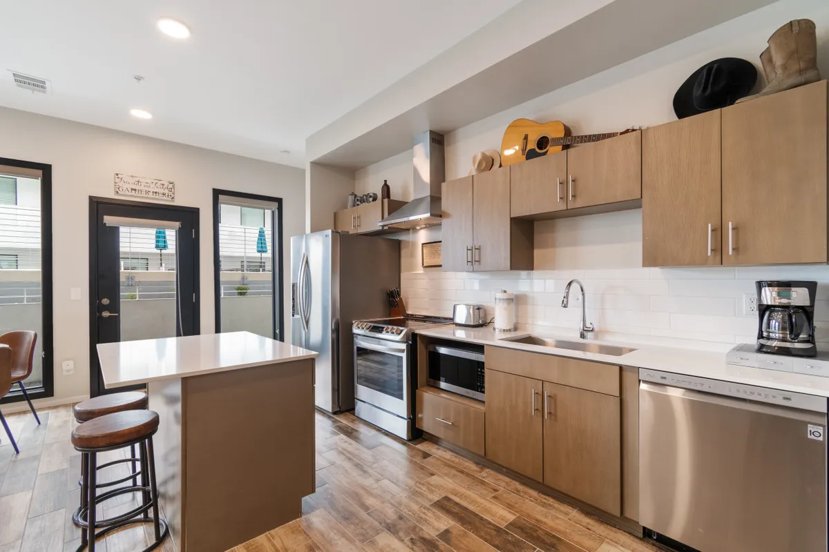 A modern kitchen with a sleek island countertop, stainless steel appliances, a guitar displayed on a shelf, and a coffee maker. The setting is warm and welcoming, suggesting opportunities for socializing, cooking, and enjoying music.
