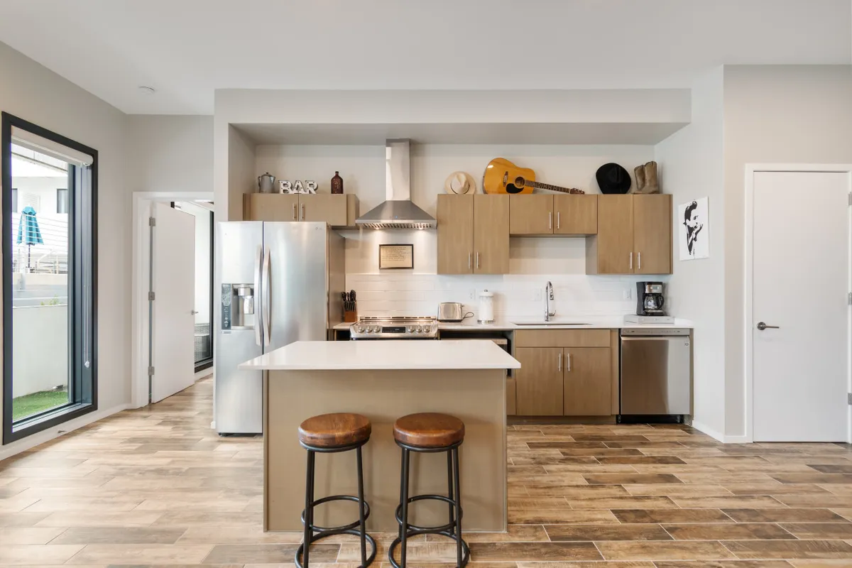 A modern kitchen with a prominent island and stools, stainless steel appliances, and a guitar hanging on the wall. The setup encourages casual dining, cooking, and musical jam sessions, with a friendly and social atmosphere.