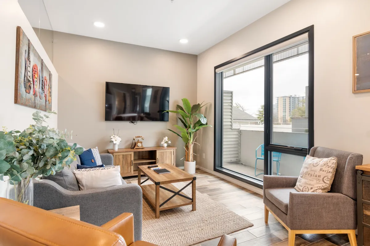A comfortable, modern living space with a TV mounted on the wall, a coffee table centered for gatherings, and greenery adding a fresh touch. Sunlight streams in, making it an inviting spot to recharge between city adventures.
